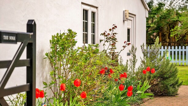 Un edificio blanco con una verja negra, rodeado de un jardín con tulipanes rojos y diversos arbustos.