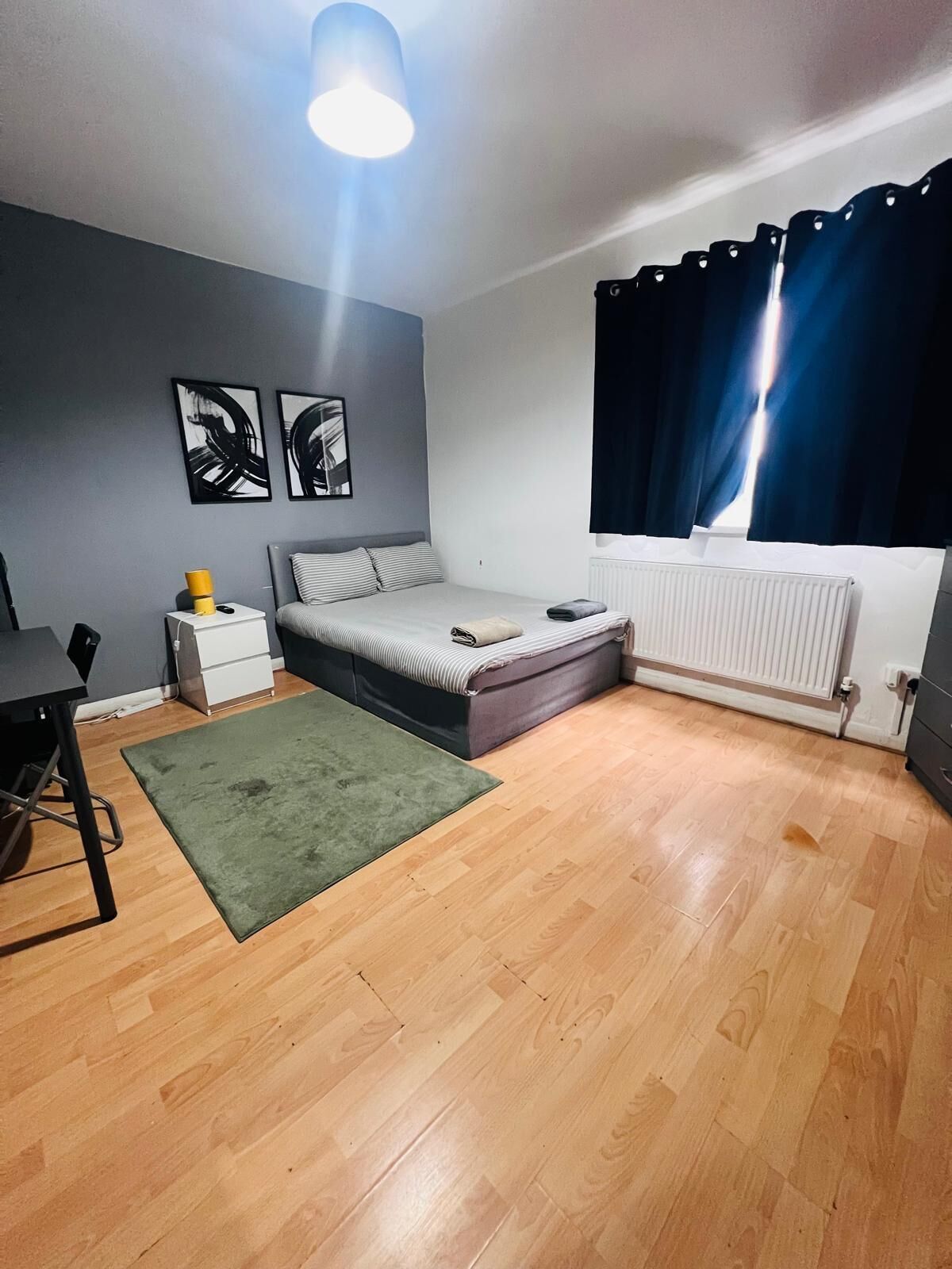 Un dormitorio con cama, escritorio, radiador y obras de arte en la pared.
