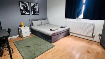 Un dormitorio con cama, escritorio, radiador y obras de arte en la pared.
