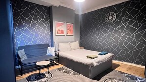 A modern bedroom with a bed, a sofa, and a small table. The room has a geometric patterned wall and a circular rug. - London E1 Hostel (London)