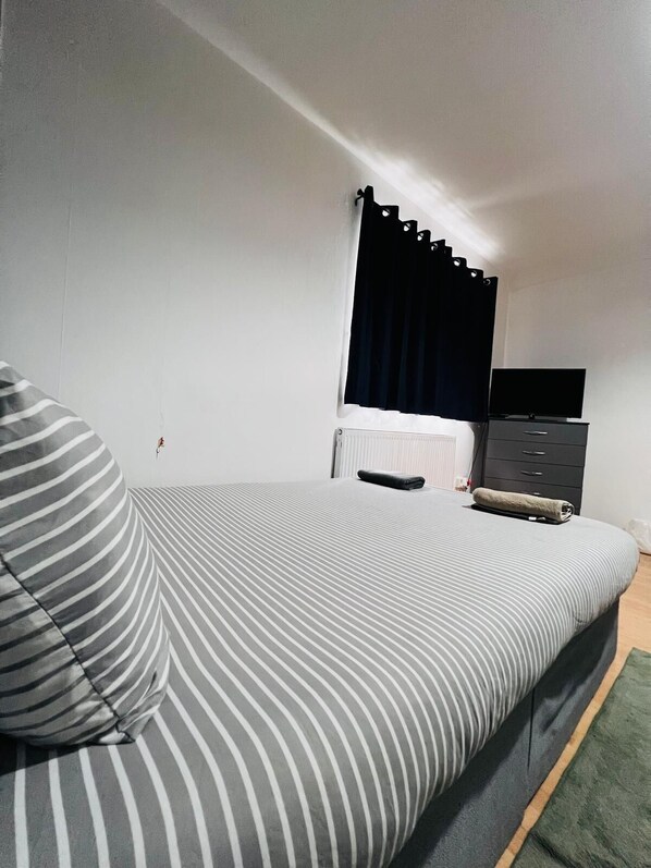 A bedroom with a bed, a TV, a dresser, and a window with curtains.