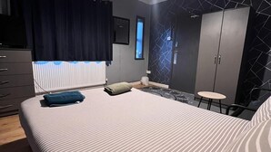 A modern bedroom with a large bed, a wardrobe, a small table, and a ceiling light. - London E1 Hostel (London)