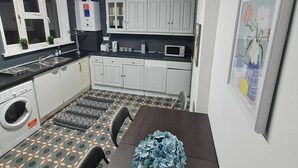 A compact kitchen with white cabinets, a built-in microwave, a water heater, and a patterned floor. - London E1 Hostel (London)