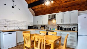 Uma cozinha moderna com armários brancos, teto de madeira e área de jantar com mesa e cadeiras de madeira.