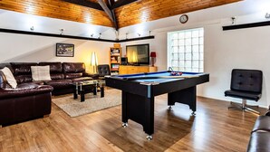 Uma sala de estar acolhedora com mesa de bilhar, sofá de couro e televisão.