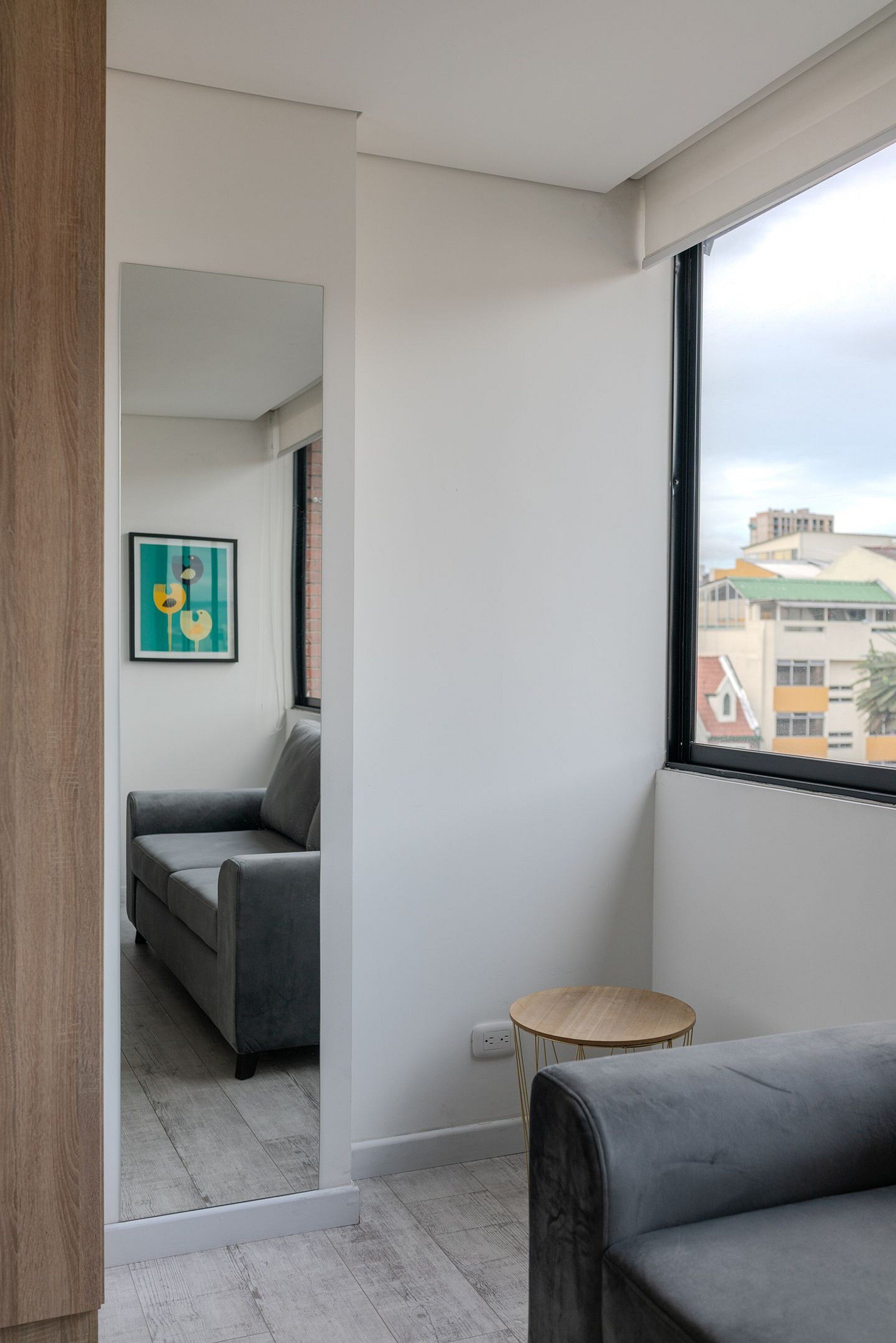 Un salon moderne avec un canapé gris, une petite table ronde en bois et un tableau abstrait encadré accroché au mur.