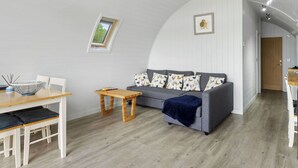 Ein moderner Loft-Wohnraum mit gewölbter Decke, einem grauen Sofa mit gemusterten Kissen, einem Holzesstisch und einem kleinen Fenster.