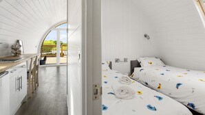 Ein stilvolles, weiß gestaltetes Zimmer mit Küchenzeile und zwei Betten mit bunter Bettwäsche.