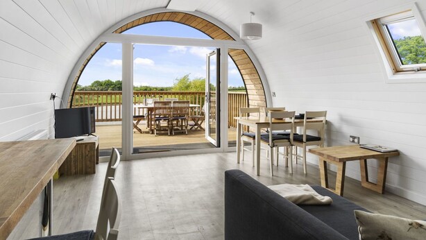 Ein gemütliches, modernes Interieur mit gewölbter Decke, einem Essbereich mit Holzmöbeln und einem großen, rundbogigen Durchgang zu einer Außenterrasse.
