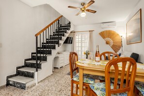 A dining area with a wooden table, chairs, a fan, and a staircase.