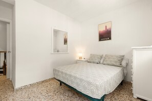 A bedroom with a bed, a nightstand, a mirror, a wall-mounted picture, and a door.