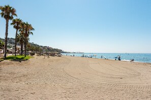 A beach with palm trees, a clear sky, and a distant view of a city.