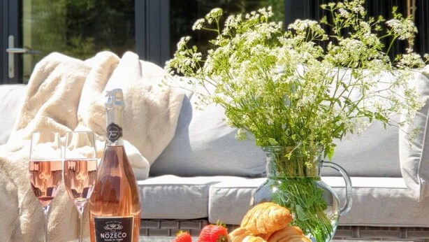 A glass table with a bottle of Nozéco wine, two glasses, strawberries, and croissants on a balcony with a view of trees and a dark building. - Beautiful  villa for 4 guests with WIFI, TV and terrace (Sawston)