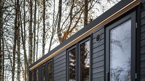 A cabin with a deck, outdoor seating, and a large window.