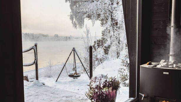 Una habitación acogedora con un ventanal amplio que da a un paisaje nevado, una chimenea y una estufa en el suelo.