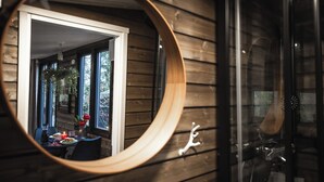 A circular mirror reflecting a dining area with a table set for two, a candle, and a vase with flowers.