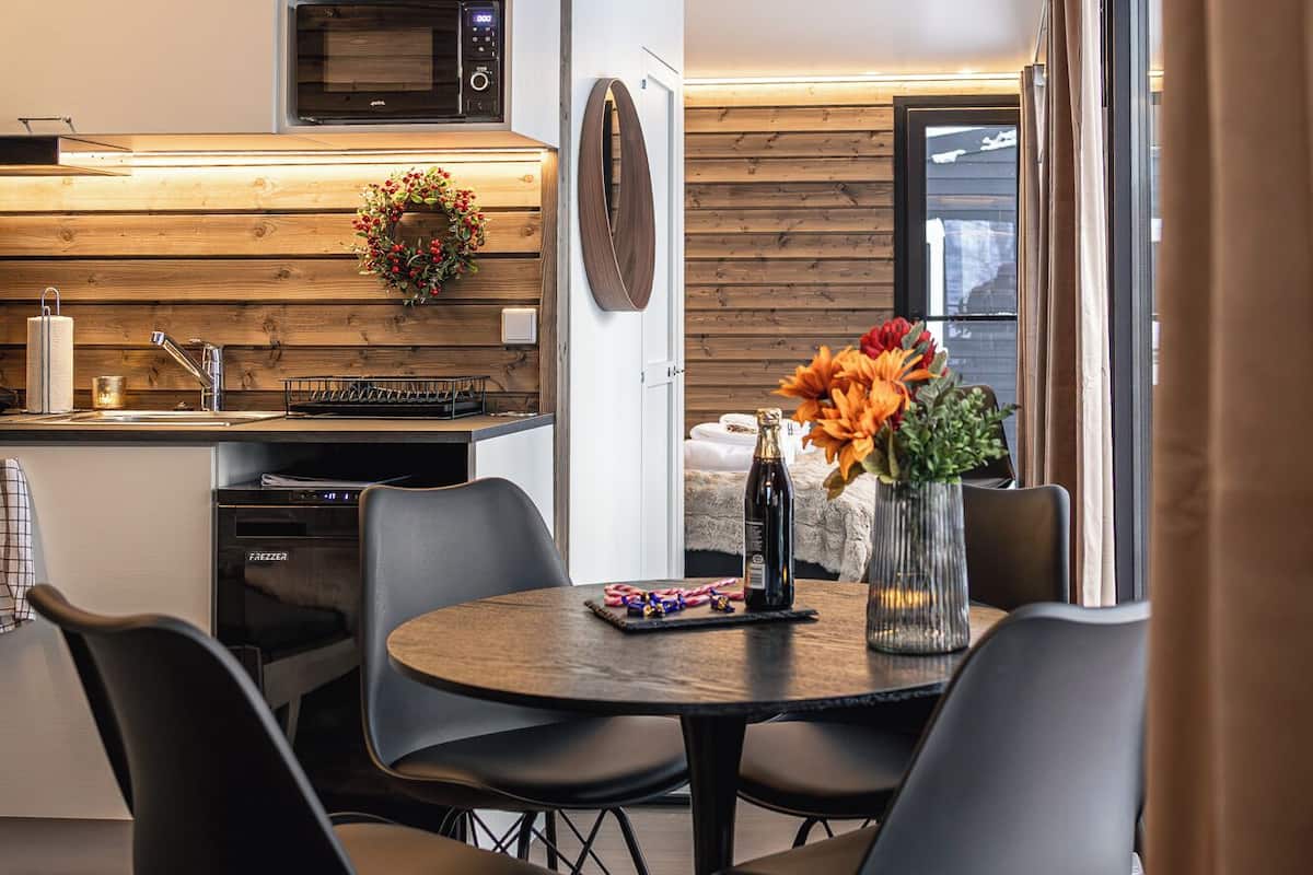 A modern kitchen with wooden cabinetry, a built-in oven, and a microwave. There is a dining area with a round table and four chairs.