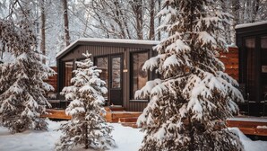 Una cabaña de madera con amplios ventanales y un paisaje cubierto de nieve.