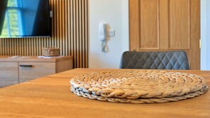 A wooden table with a woven placemat, a television mounted on a wall with vertical blinds, and a wooden door in the background. - Nice apartment for 2 guests with WIFI and TV (Matlock)