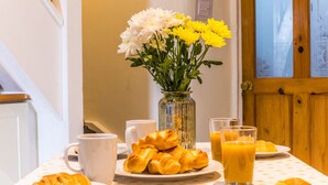 A breakfast table with croissants, a vase of flowers, and a glass of orange juice.