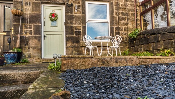 A stone building with a green door, a window, and a white outdoor seating area with chairs and a table.