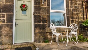 A stone building with a green door, a window, and a small outdoor table with chairs.