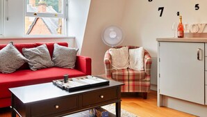 A cozy room with a red sofa, a plaid armchair, a small table, and a cabinet.
