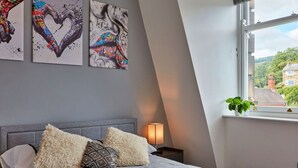 A bedroom with a bed, pillows, a bedside lamp, and artwork on the wall.