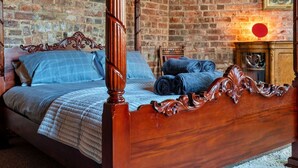A four-poster bed with a wooden headboard, a brick wall background, and a fireplace with a red-glowing element. - Beautiful  villa for 9 people with WIFI, TV, terrace and pets allowed (Hickleton)