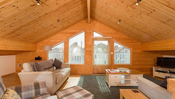 Ein gemütliches Blockhaus mit hohen Decken, einer Couch, einem Couchtisch und einem Fernseher.