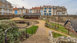 A coastal promenade with a stone pathway leading to a gazebo, surrounded by colorful terraced houses and a stone wall. - Beautiful  villa for 2 guests with pets allowed (Cromer)