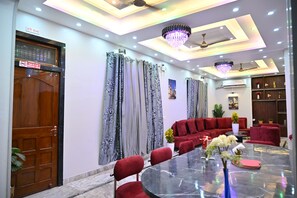 Une chambre d’hôtel avec un coin repas, un canapé rouge, un lustre et un ventilateur de plafond.