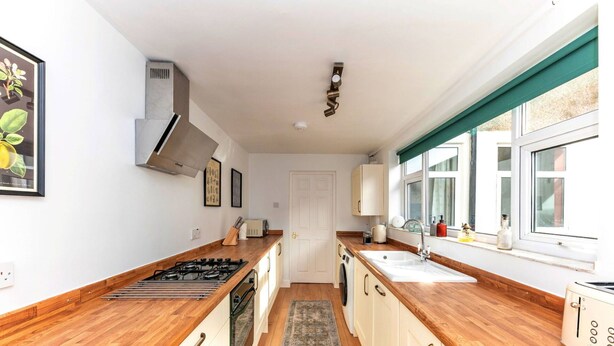 A modern kitchen with wooden countertops, a built-in oven, a sink, and a window with curtains.