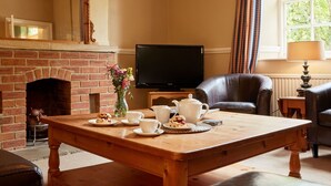 A cozy living room with a brick fireplace, a television, a leather armchair, and a wooden coffee table with tea cups and pastries. - Stunning  villa for 10 guests with WIFI and TV (Belper)