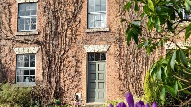 A brick building with multiple windows and a green door, surrounded by a well-maintained lawn and purple flowers in the foreground. - Stunning  villa for 10 guests with WIFI and TV (Belper)