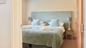 Een netjes opgemaakt bed met een lichtblauwe hoofdbord, twee bedlampen en een hangende lamp.