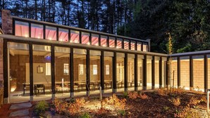 Een modern gebouw met grote glasramen en een gevel van natuursteen, omringd door een aangelegde tuin met bomen en struiken.