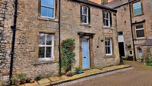 A stone building with multiple windows and doors, a cobblestone street, and a small garden area with potted plants.