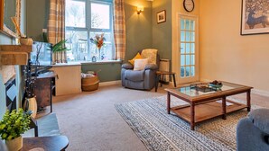 A cozy living room with a fireplace, a comfortable sofa, a coffee table, and a large window with curtains. - Beautiful  villa for 4 guests with WIFI, TV and pets allowed (Matlock)