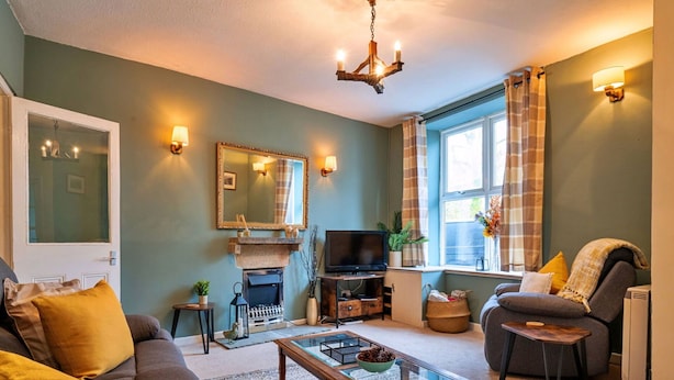 A living room with a sofa, coffee table, TV, fireplace, and a window with curtains. - Beautiful  villa for 4 guests with WIFI, TV and pets allowed (Matlock)