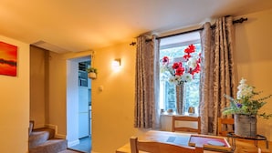 A dining area with a wooden table, chairs, a rug, a window with curtains, and a vase with flowers. - Beautiful  villa for 4 guests with WIFI, TV and pets allowed (Matlock)