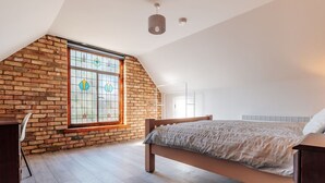A bedroom with a sloped ceiling, a large window with stained glass, a bed, and a desk. - Stunning  villa for 4 guests with WIFI (Ramsey)