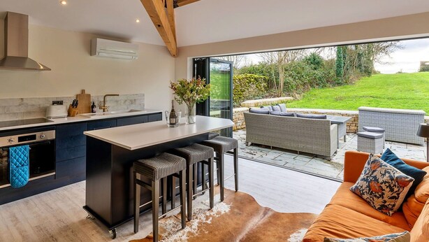A modern kitchen with a central island, bar stools, and a dining area with outdoor seating.