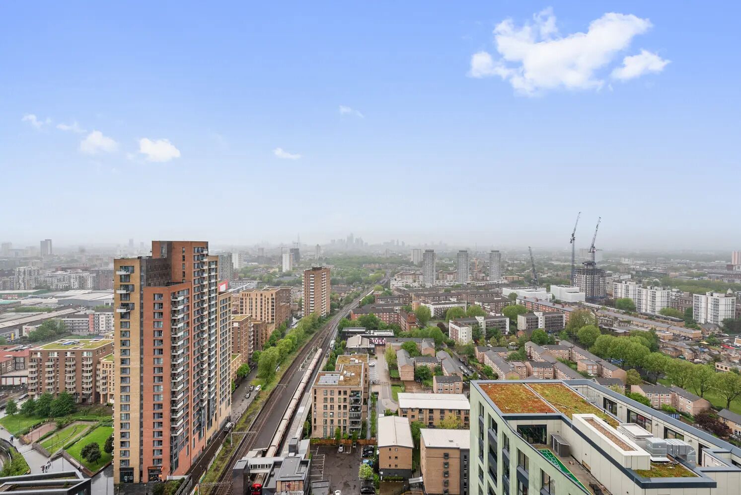 Een hoog gebouw met meerdere verdiepingen, omringd door andere woon- en bedrijfsgebouwen, met een heldere lucht en een verafgelegen stadsachtergrond.