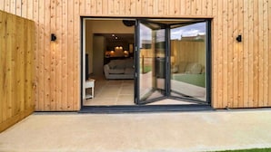 Un bâtiment moderne doté d’une façade en bois et d’une porte coulissante en verre qui donne sur un espace intérieur comprenant un canapé et un coin repas.