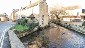 A narrow waterway with stone buildings on either side, a small bridge, and a grassy area with a pathway.
