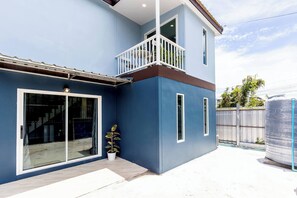 Una casa a due piani con un balcone, ampie porte scorrevoli in vetro e una pianta in vaso.