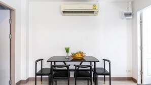 Un comedor con una mesa y cuatro sillas, un aire acondicionado montado en la pared y un ventanal pequeño.
