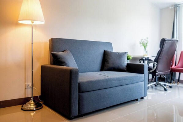 A modern office chair, a sofa, and a floor lamp in a well-lit room with a tiled floor.