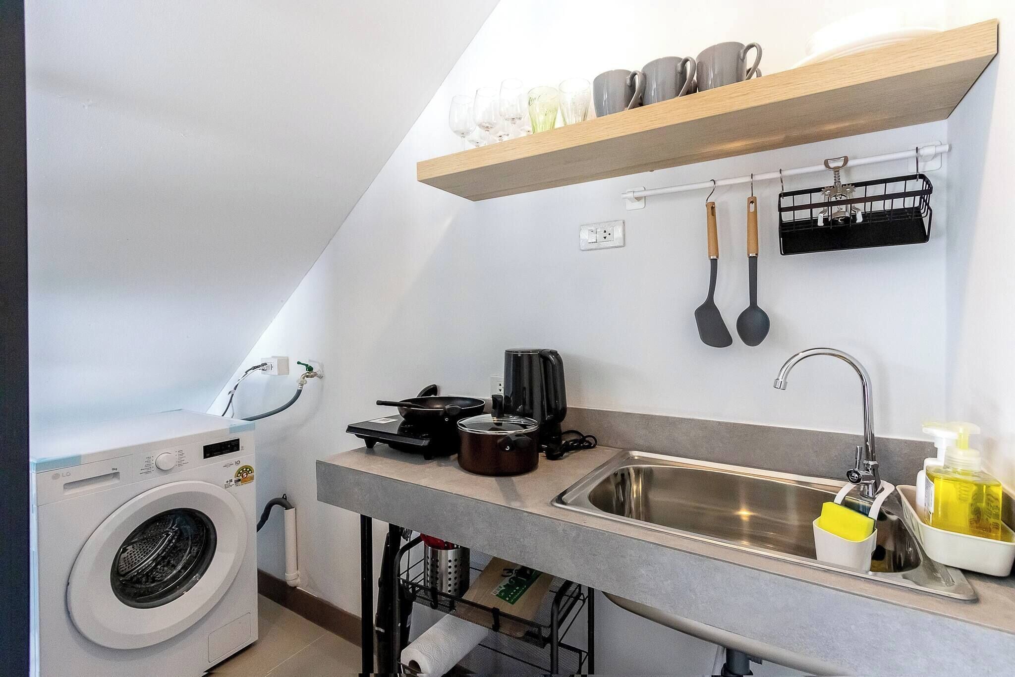 A compact kitchen with a washing machine, a sink, and a countertop with a kettle, a toaster, and a bottle of dish soap.